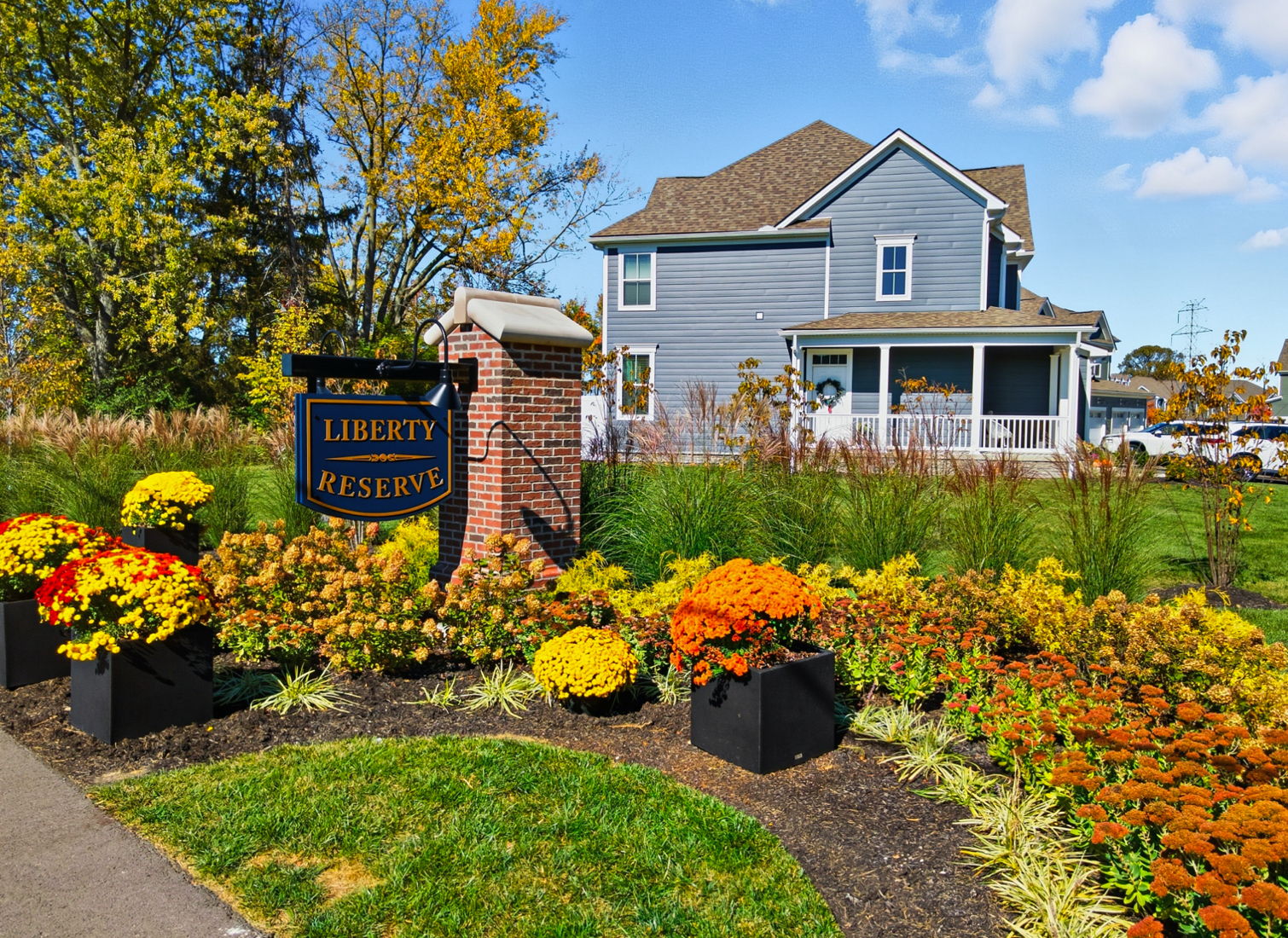 Blue two-story townhome exterior at Liberty Reserve in Powell, Ohio, featuring private front porch, attached garages, and landscaped front lawn.