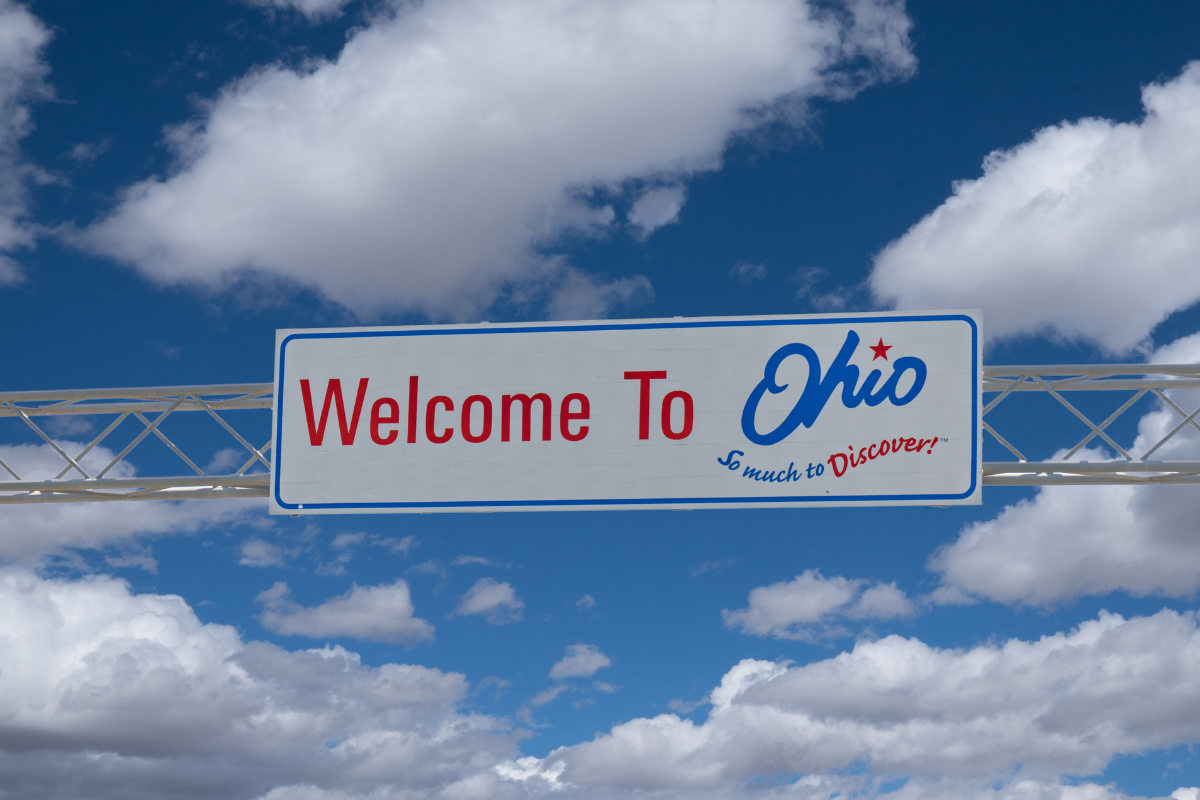 Welcome to Ohio sign along the highway with blue sky and clouds overhead.