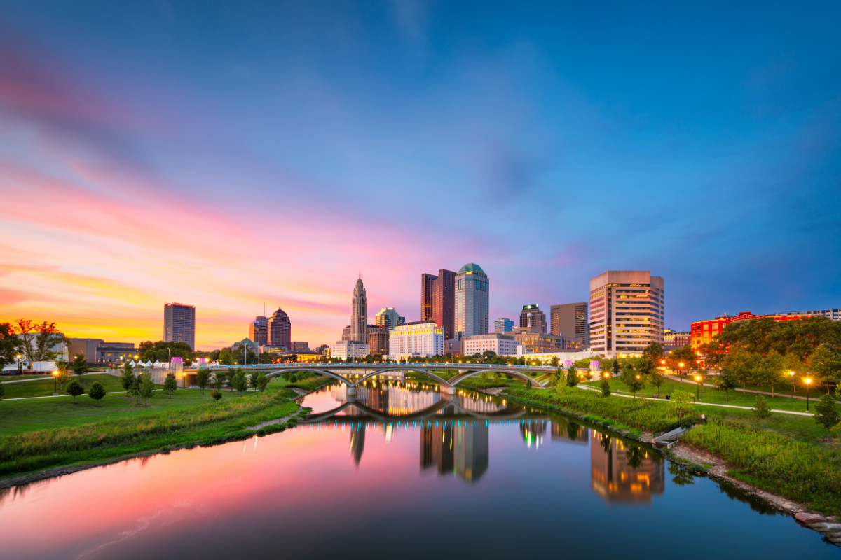 Columbus, Ohio skyline at sunset overlooking the Scioto River and downtown buildings.