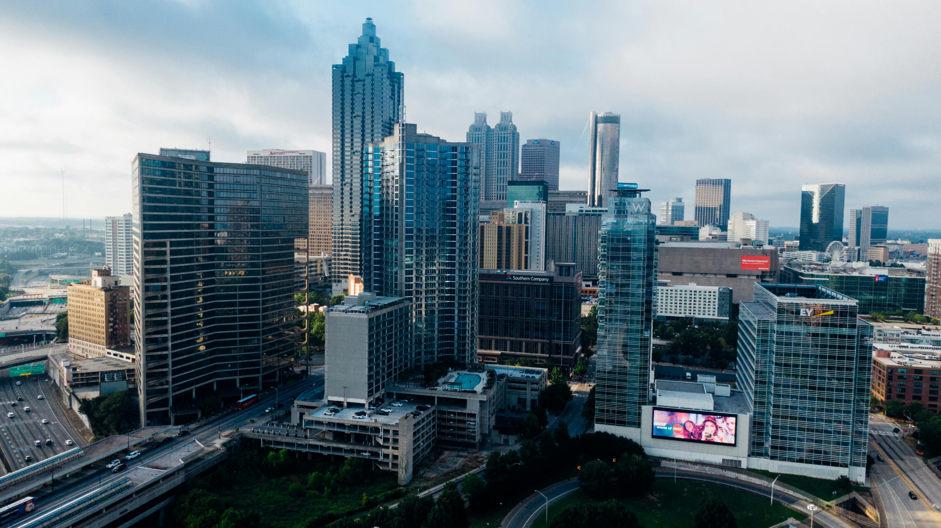 Tall modern glass skyscrapers overlooking a busy highway winding through a sprawling downtown city skyline.