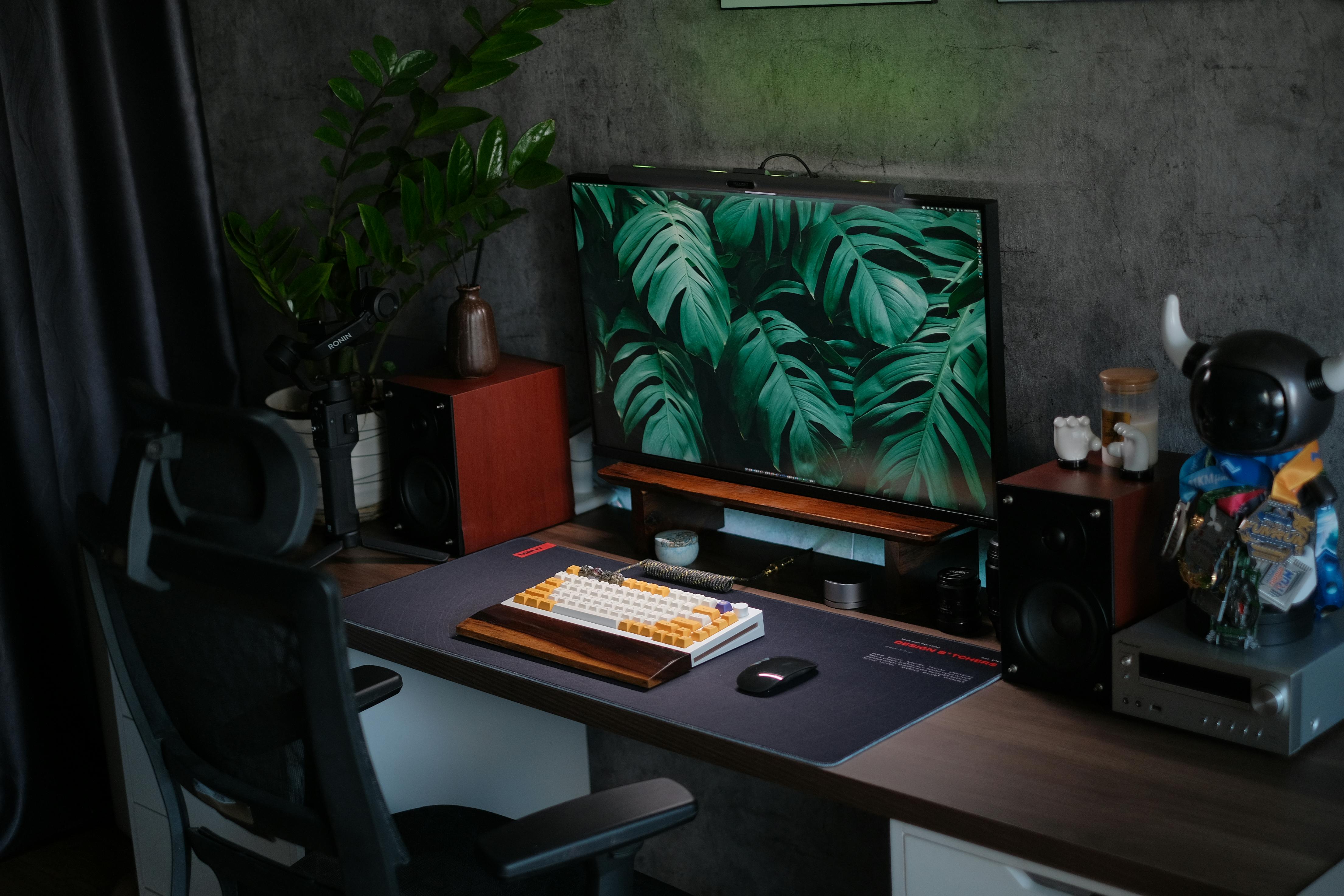 A computer monitor displaying green leaves resting on a wooden desk near a mechanical keyboard and wooden speakers.