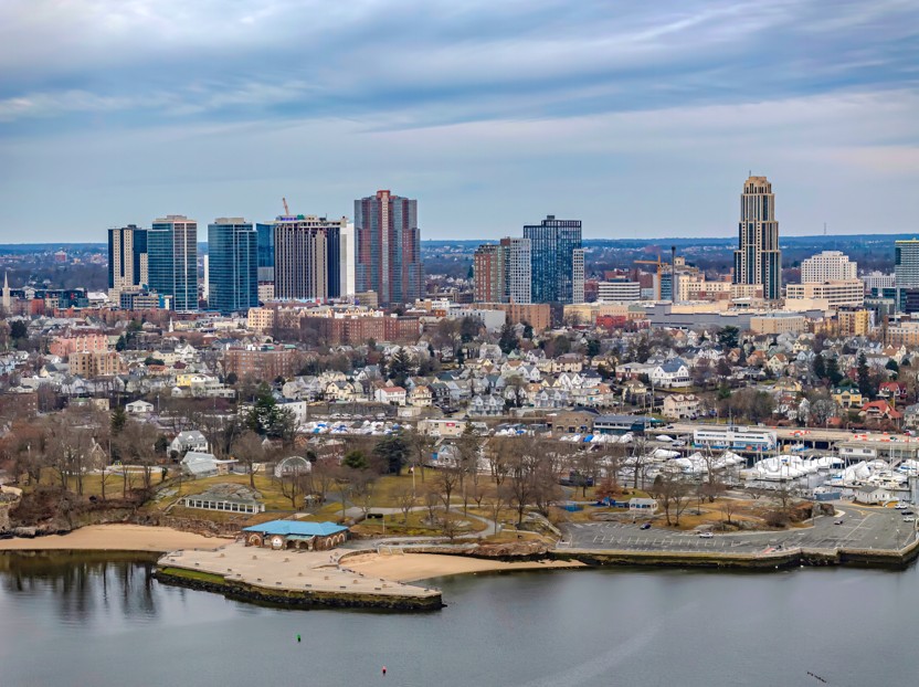 Skyline of New Rochelle, New York, featuring high-rise buildings overlooking a waterfront park and harbor.