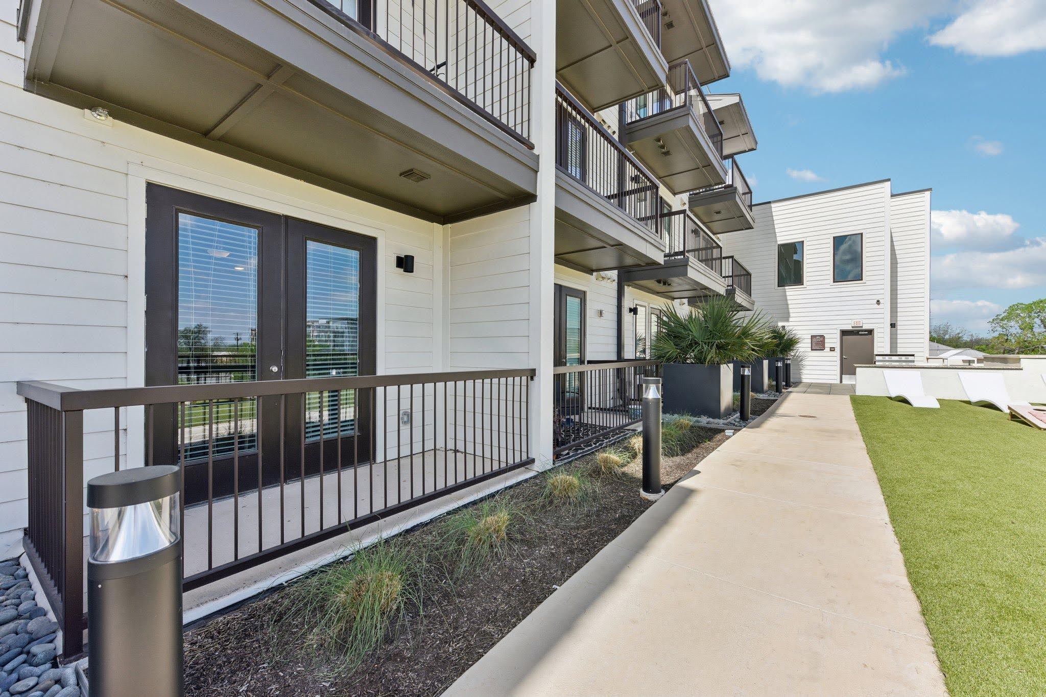 Ground-floor apartment patios with black metal railings along a landscaped walkway at a South Austin community
