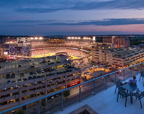 Rooftop terrace at dusk where a resident sits overlooking the lit ballpark and surrounding streets in the Navy Yard and Ballpark District