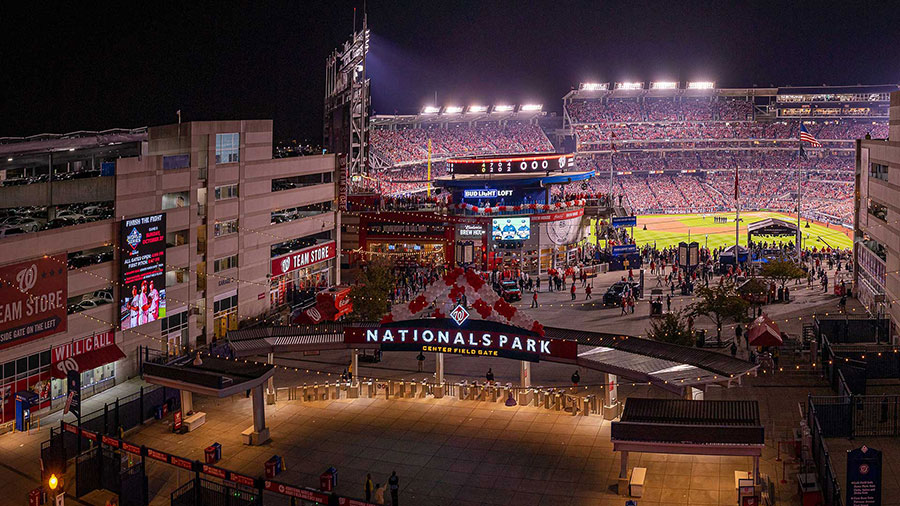 Aerial night view of Nationals Park and the Navy Yard neighborhood in Washington, D.C., showing the ballpark lit up on game night surrounded by the walkable mixed-use district