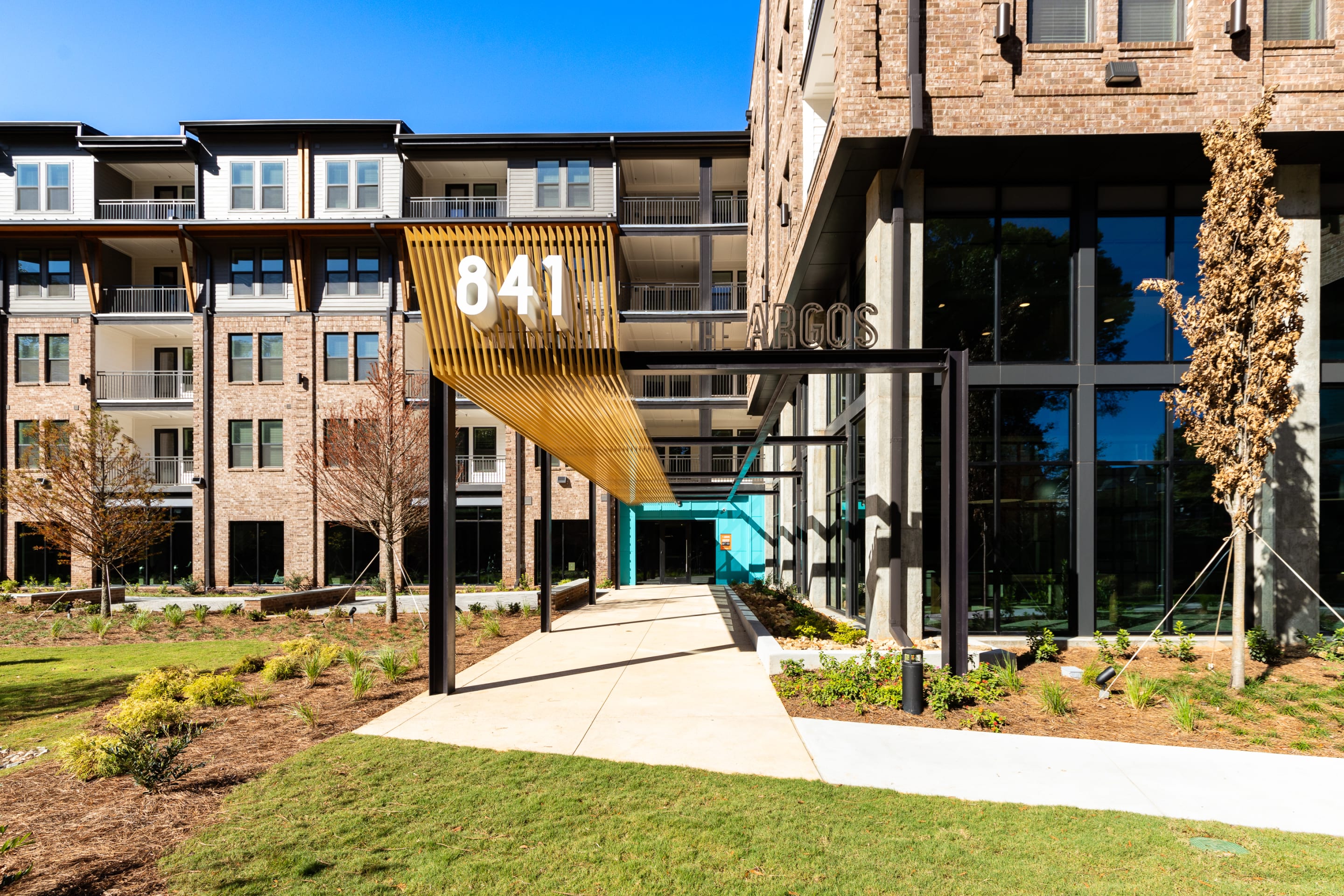 Exterior entrance of The Argos Apartments at Grant Park- a luxury apartment complex with brick facades, large windows, landscaped walkway, and bold 841 canopy.