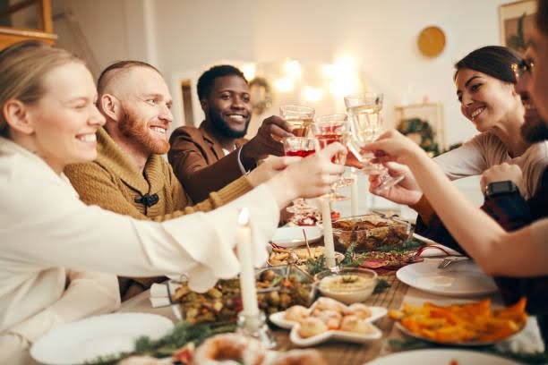 A group of friends at Wesley St. Claire smiling, clinking wine glasses over a festive dinner table adorned with food, candles, and garlands.