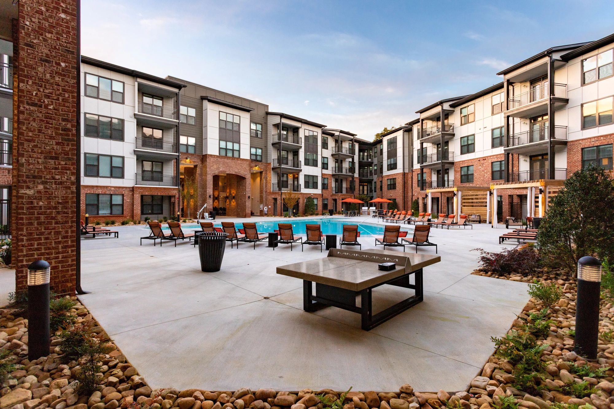 A concrete ping pong table standing in an outdoor courtyard near a bright blue swimming pool and brick buildings.