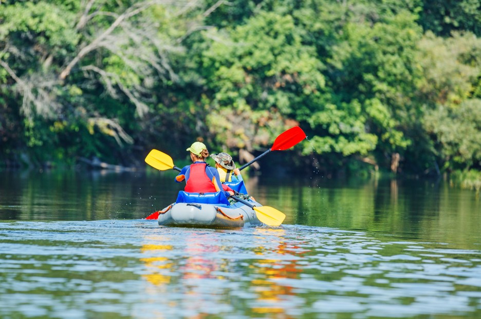 Two people kayaking on a calm river surrounded by lush green trees at Graham Creek Nature Preserve in Foley, Alabama.