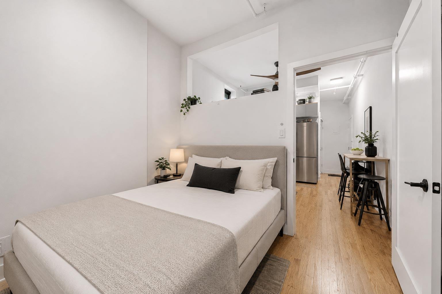 A bedroom with a bed, a chair, and a small table with a plant on it.