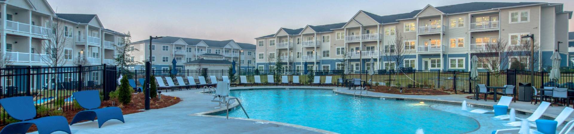 A swimming pool surrounded by blue chairs in front of apartment buildings.