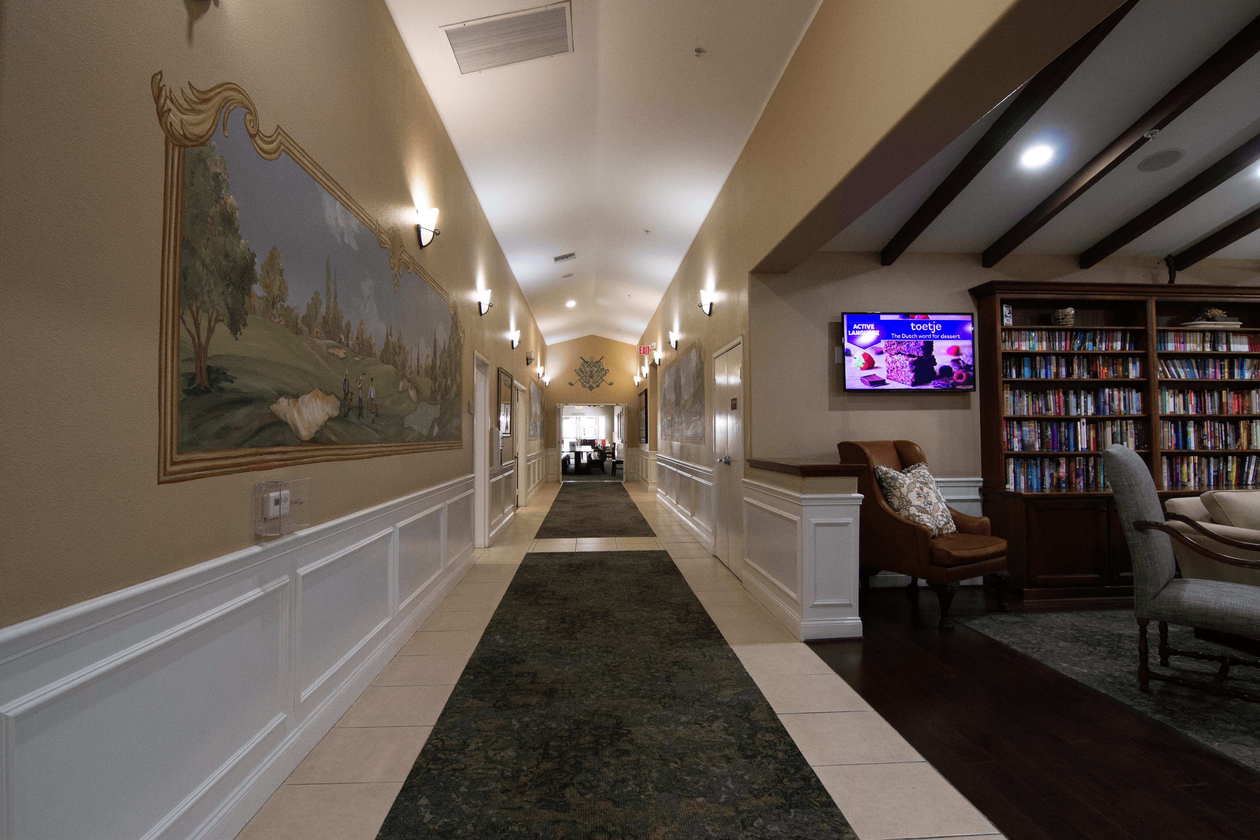 A long hallway with a painting on the wall and a TV on the wall.,A long hallway with a painting on the wall and a TV on the wall.