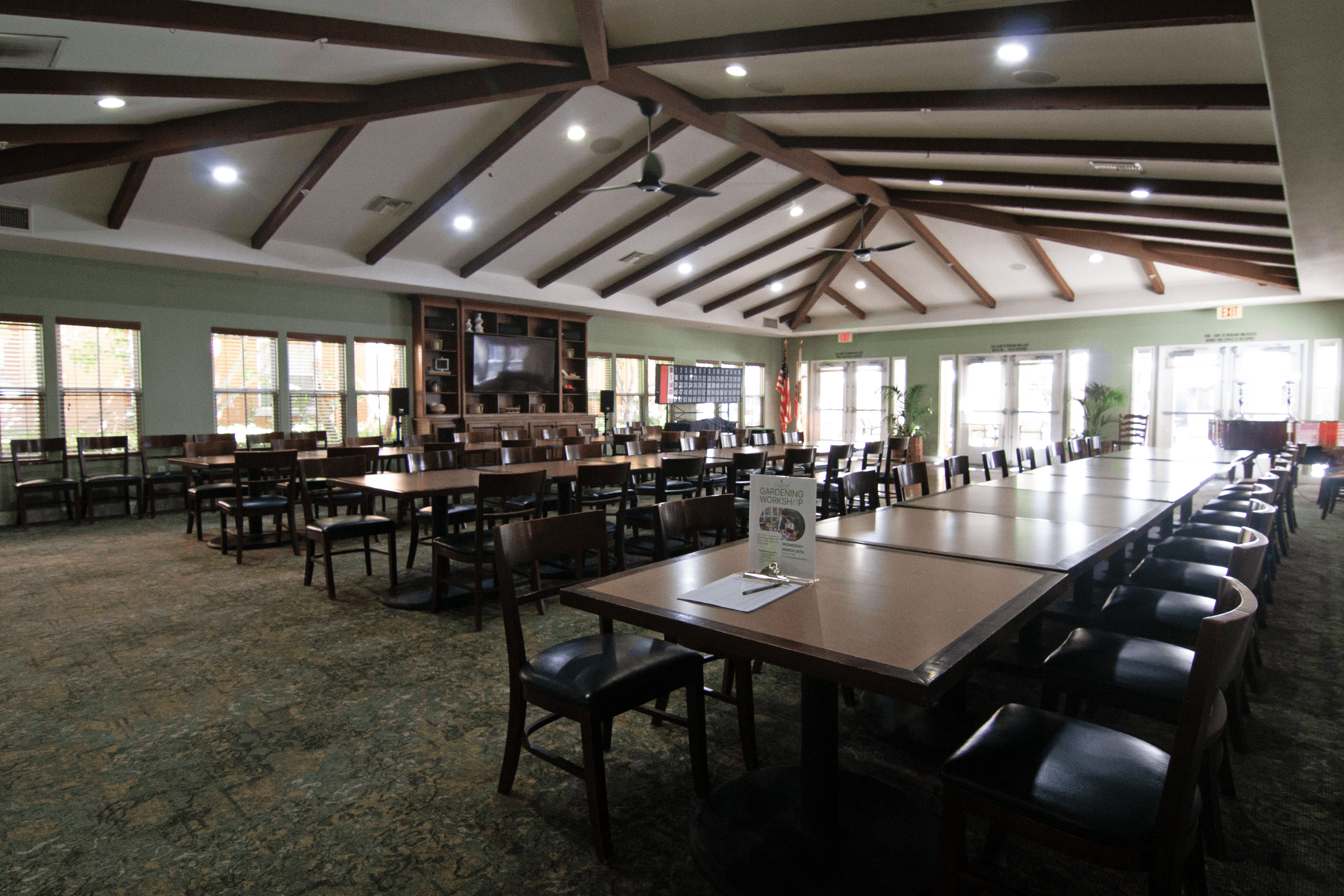 A large room with tables and chairs and a screen tv.,A large room with tables and chairs and a screen tv.