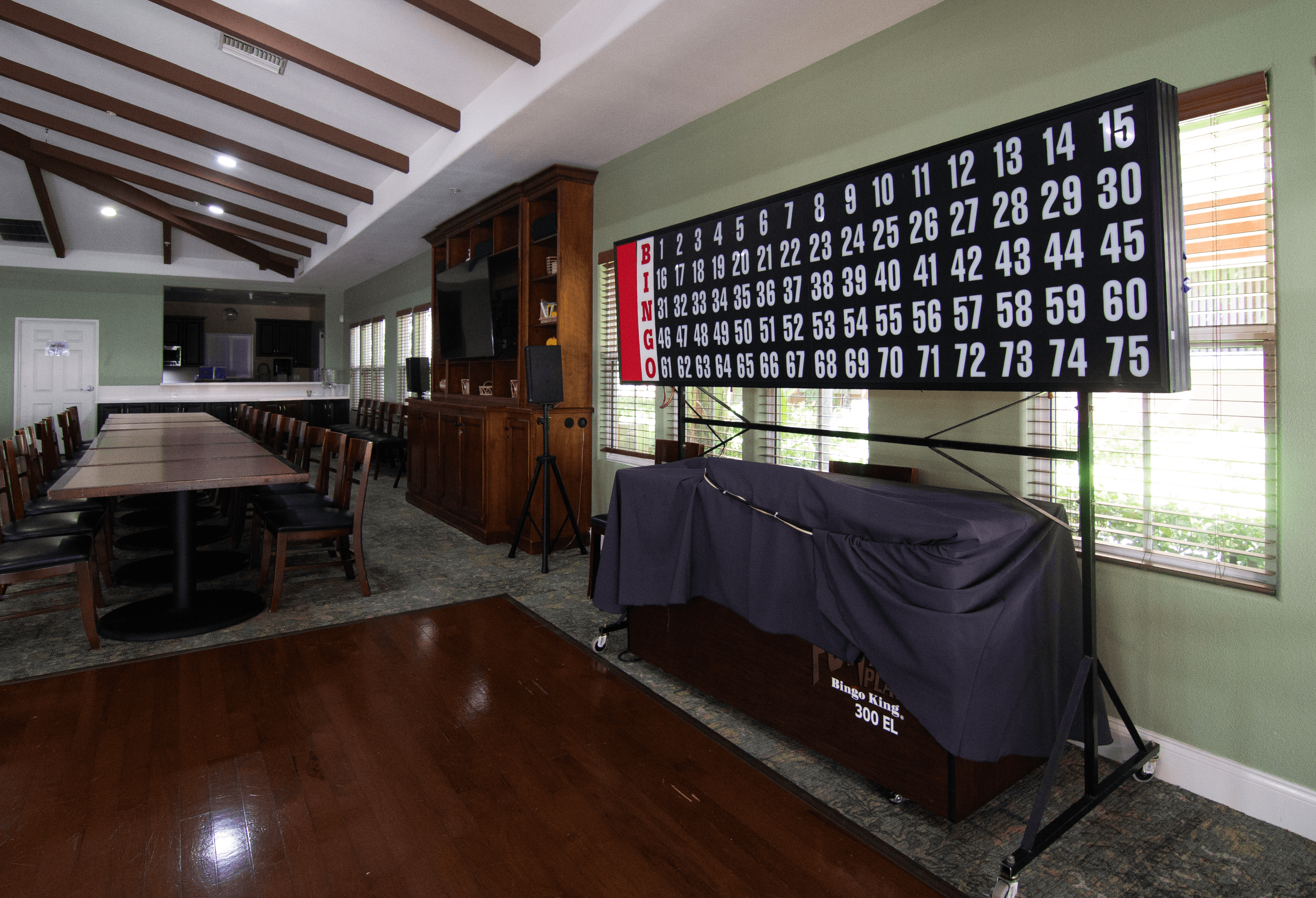 A large room with a long table and chairs, a projector screen, and a wall with numbers from 1 to 75.,A large room with a long table and chairs, a projector screen, and a wall with numbers from 1 to 75.