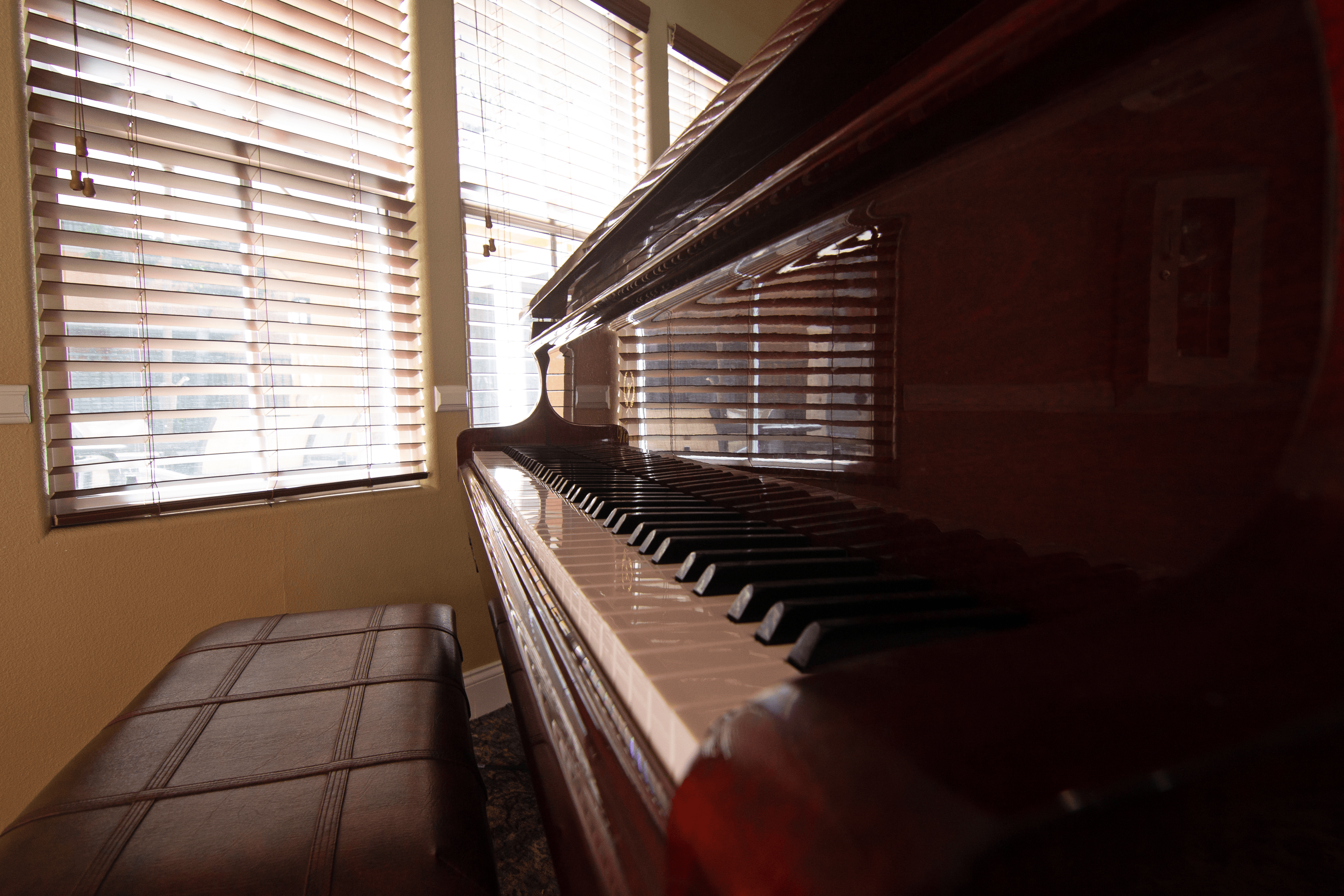 A brown piano sits in front of a window with blinds.,A brown piano sits in front of a window with blinds.