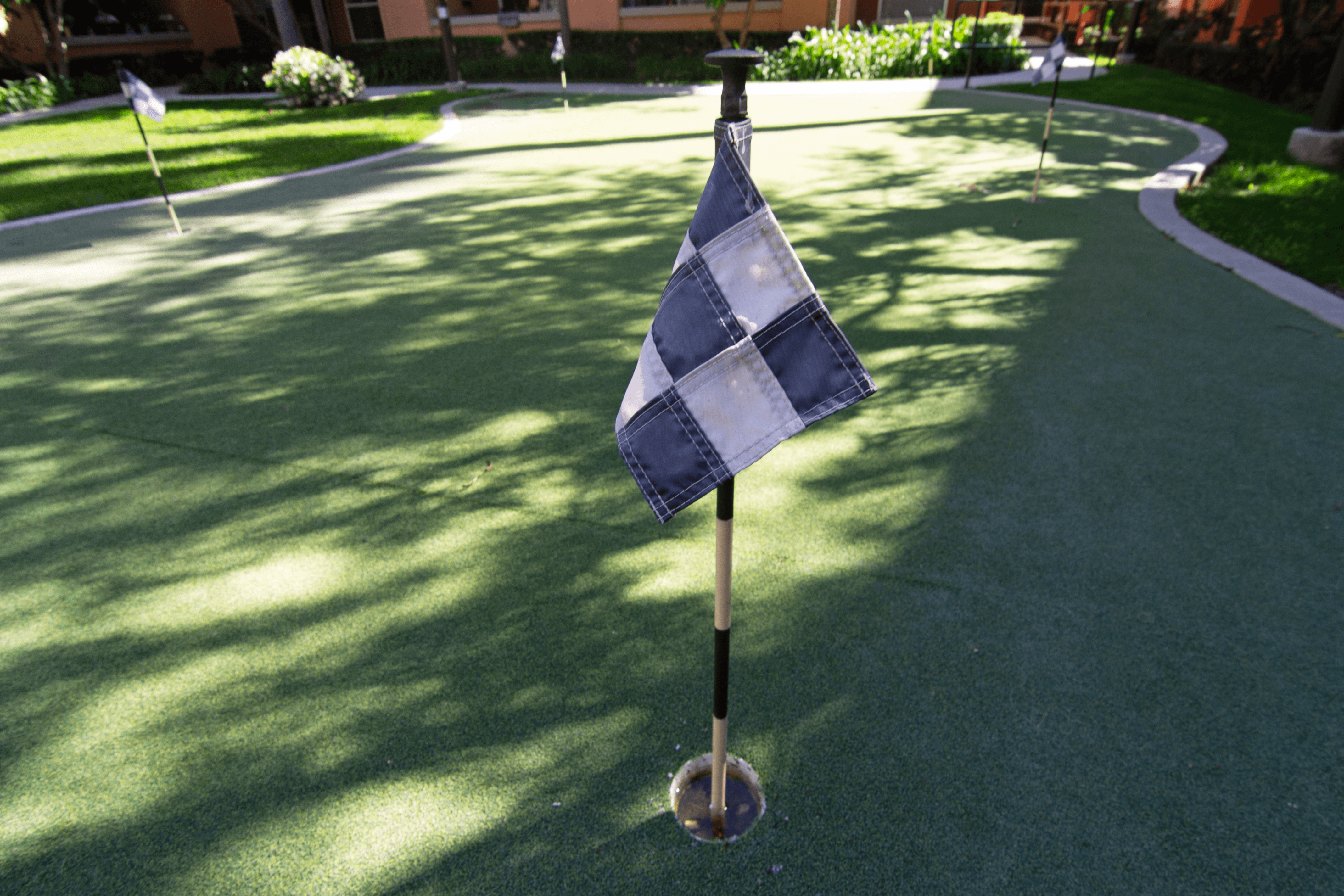 A blue and white checkered flag on a pole in the middle of a green lawn.,A blue and white checkered flag on a pole in the middle of a green lawn.