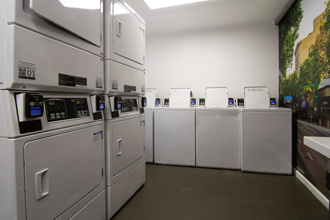 A row of industrial washing machines are lined up in a laundromat.