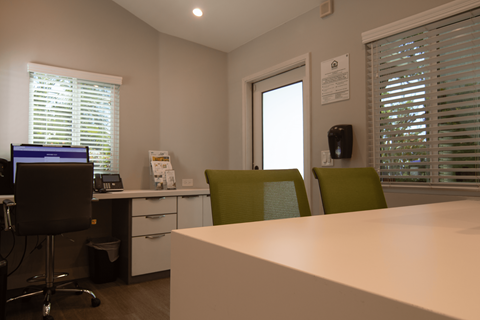 A white desk with a computer and two chairs in front of a window.