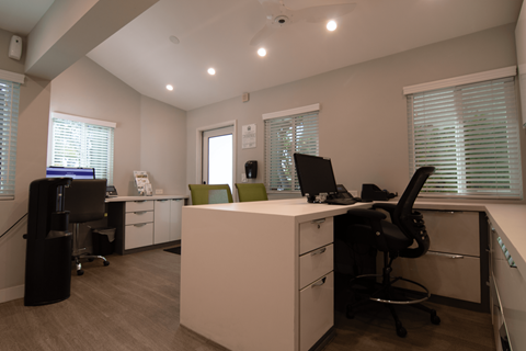 A white reception desk with a black chair in front of it.