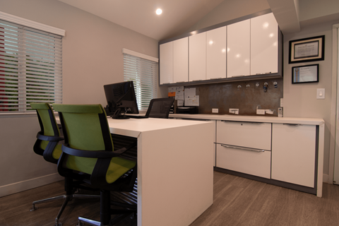 A white desk with a green chair in front of a white cabinet.