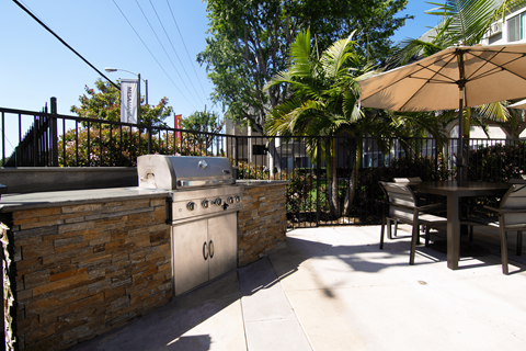A patio with a grill and chairs under an umbrella.