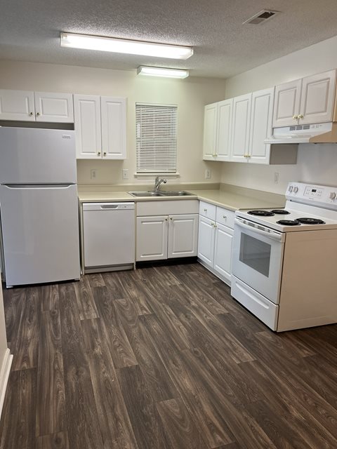 A kitchen with white appliances and wooden floors.