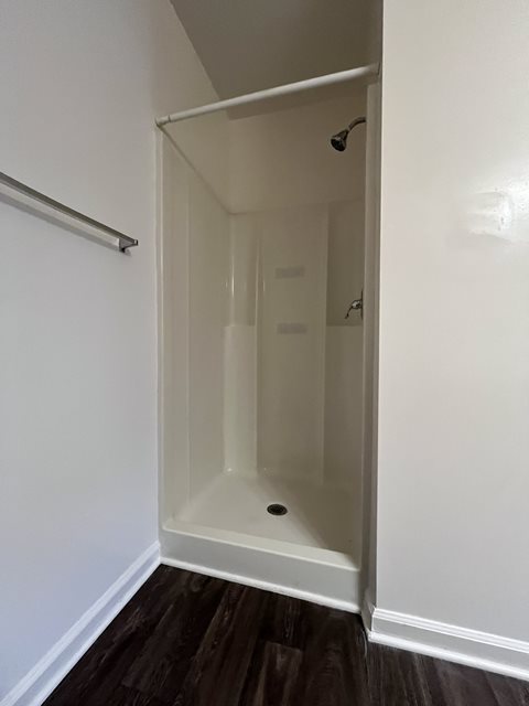 A white bathroom with a shower stall and a wooden floor.