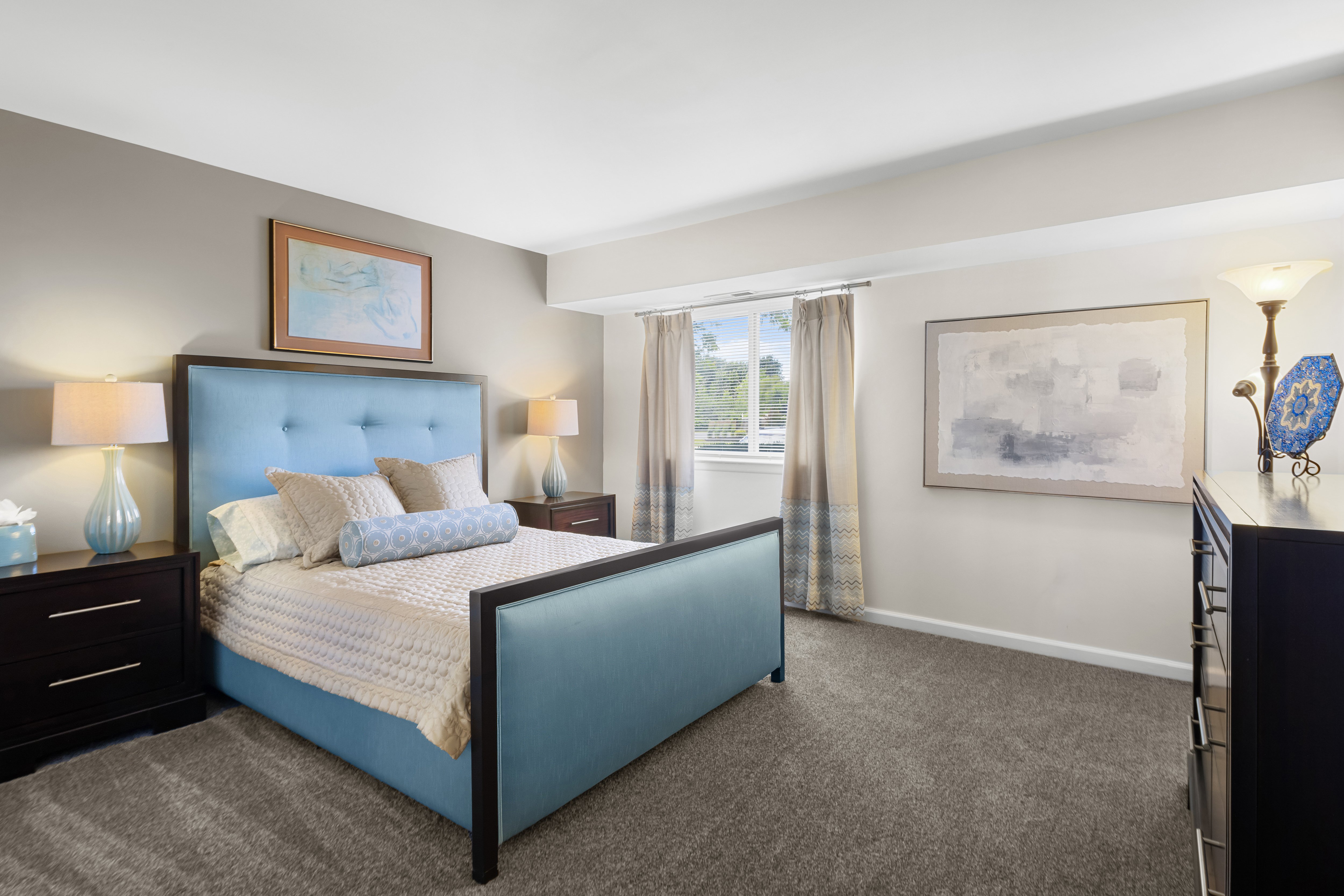 A bedroom with a blue bed and a painting on the wall.