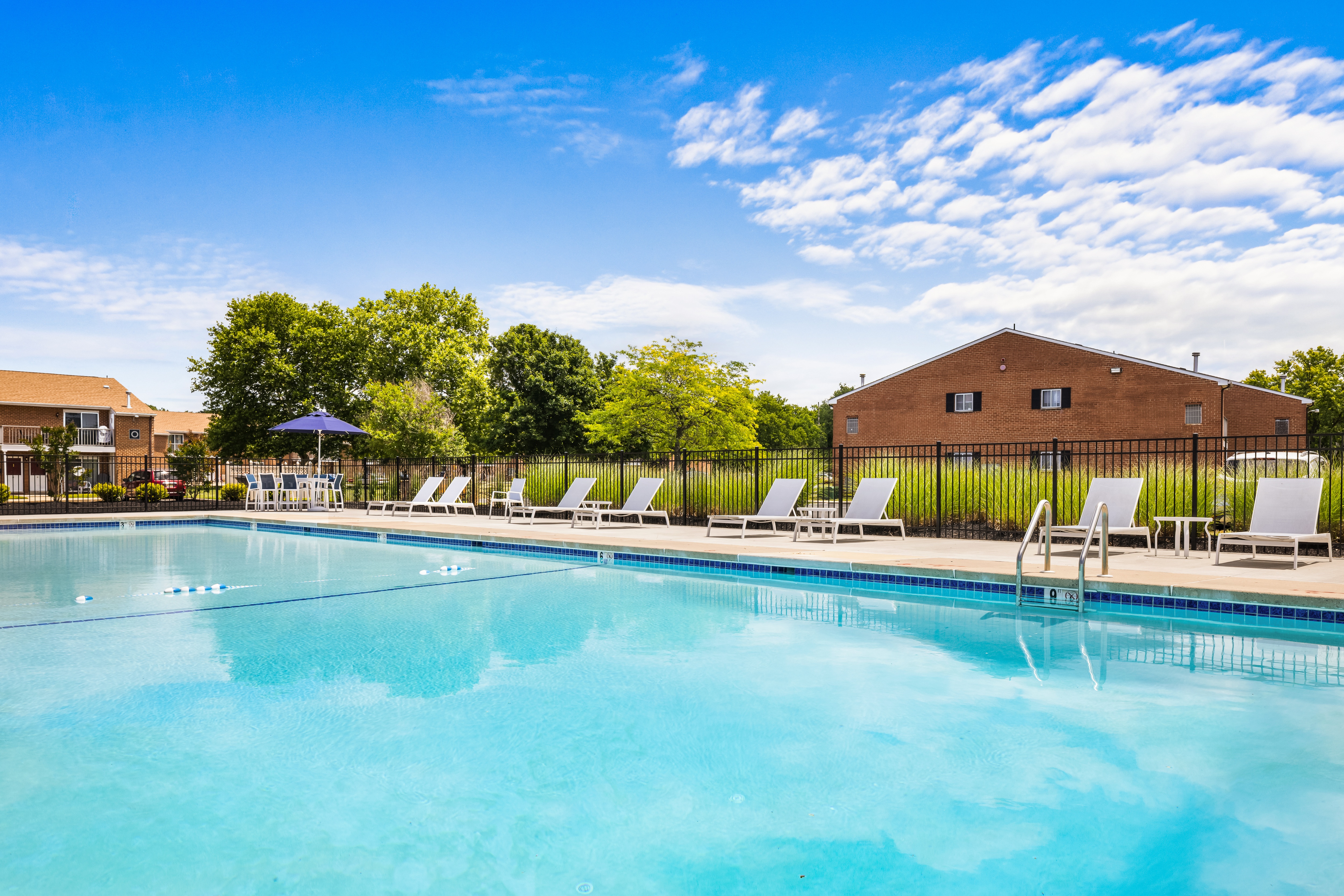 A large apartment swimming pool with lounge chairs and a clubhouse in the background.