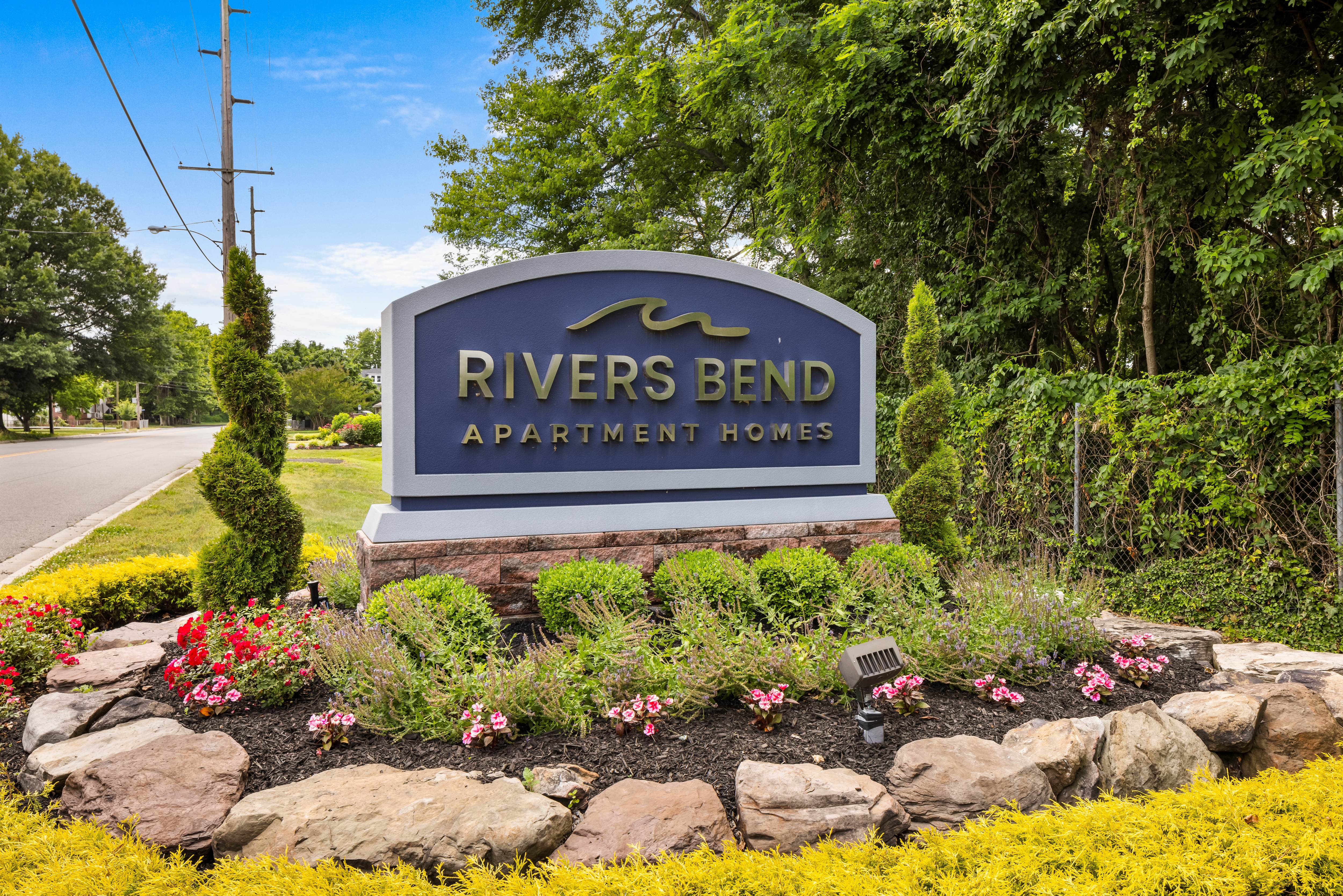 A sign for Rivers Bend Apartment Homes is surrounded by flowers and greenery.