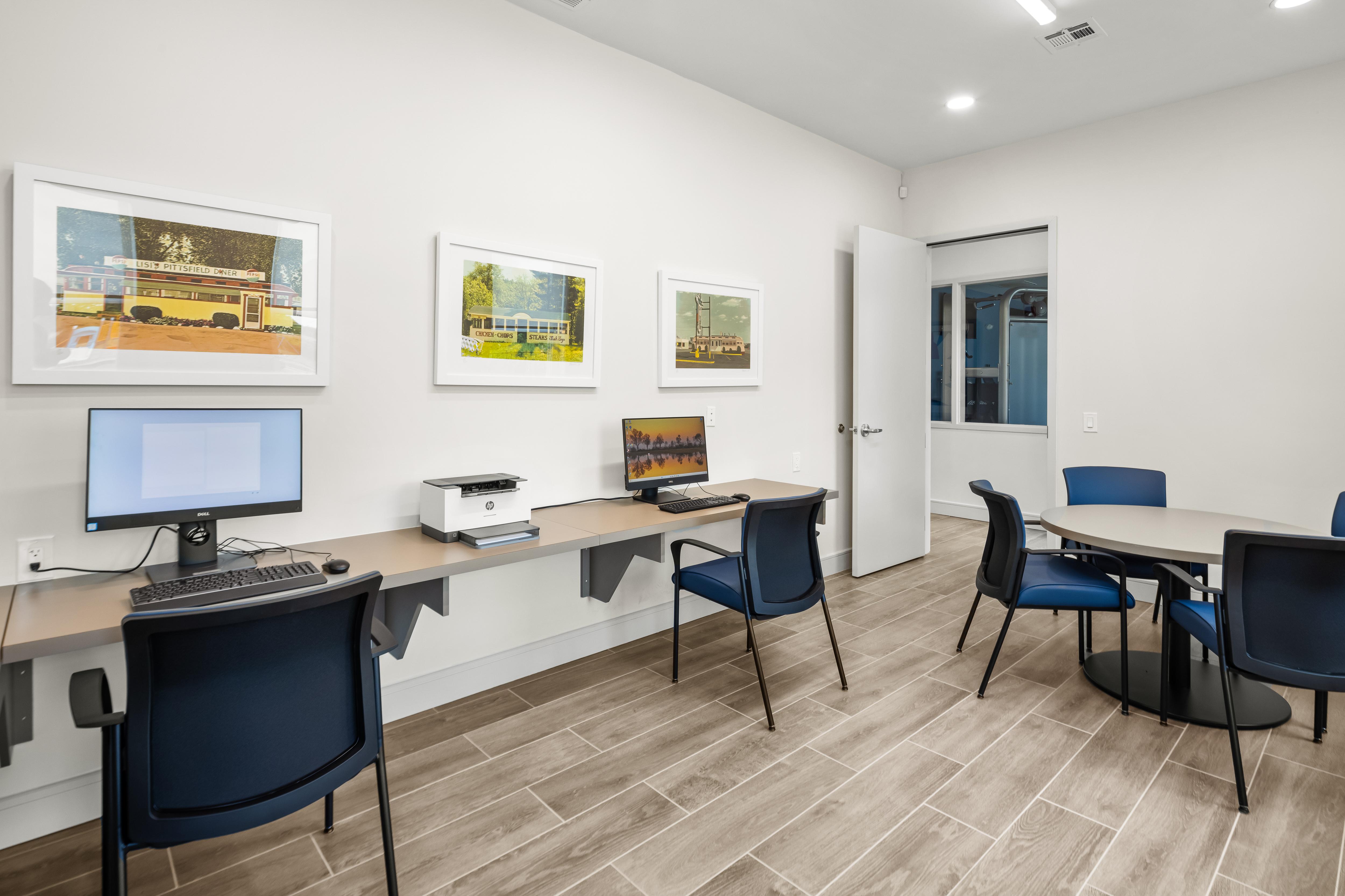 A room with a desk, chairs, and pictures on the wall.