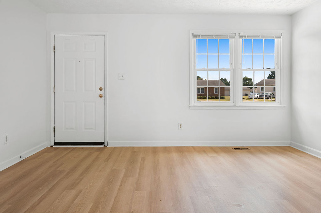 A room with a white door and a window with a view of a house across the street.