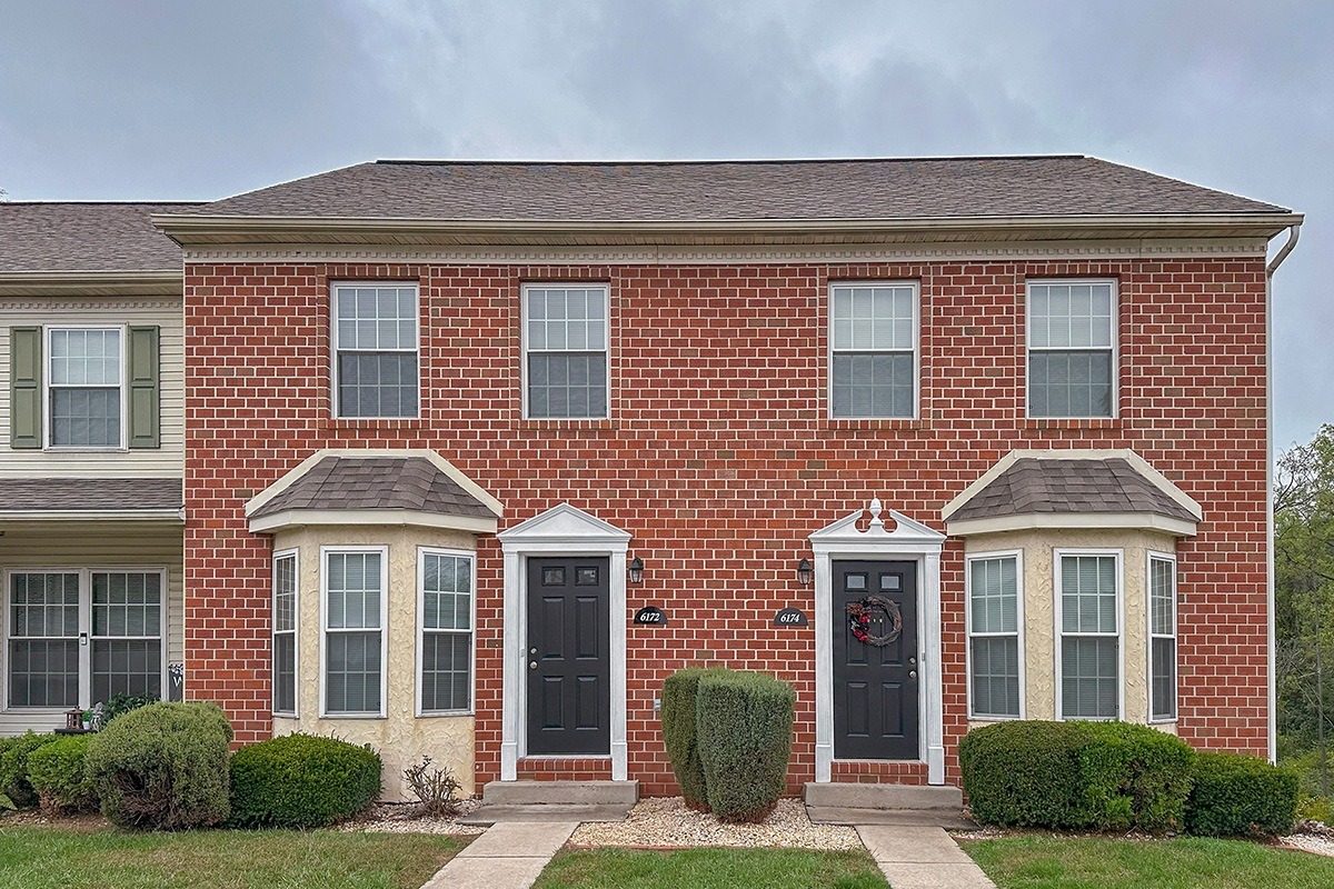 A red brick house with a black front door and two windows on either side of the door.
