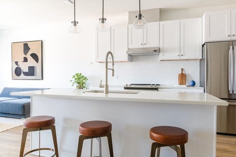 Apartment kitchen with white cabinets, leather bar stools, a Moen faucet and tile backsplash