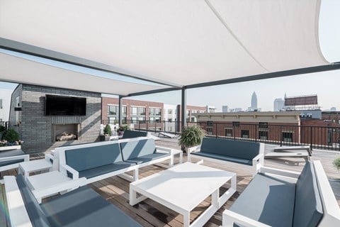 Rooftop lounge featuring couches, awning, television and fireplace. Downtown Cleveland can be seen in distance.