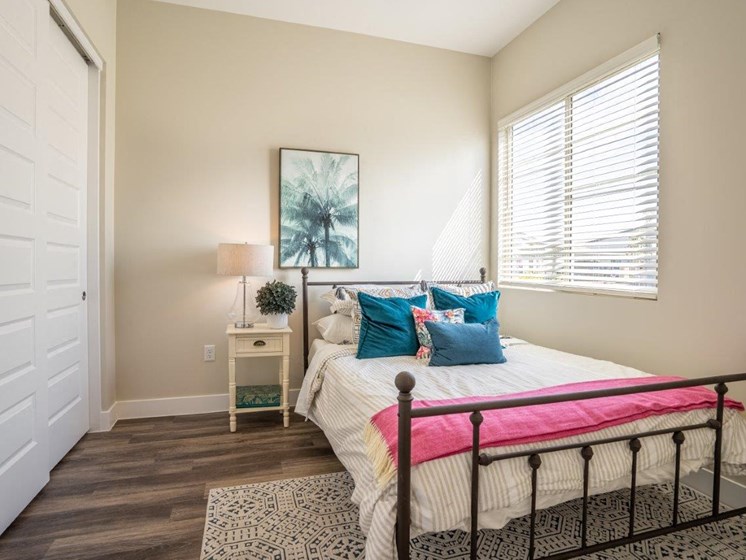 A large bed with a nightstand sits in a bedroom with double closet doors and a window at Village Greens of Queen Creek