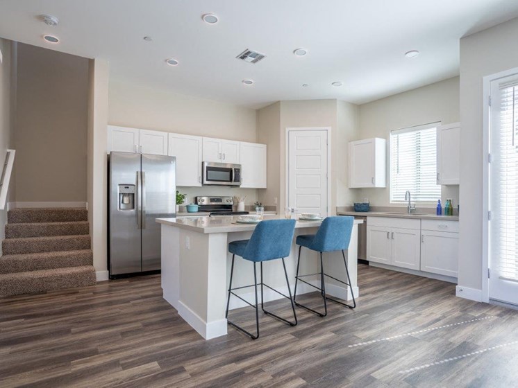 An open concept kitchen has an island with two stools in an apartment at Village Greens of Queen Creek
