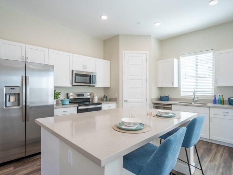 An island with 2 stools sits in the middle of a kitchen with stainless steel appliances at Village Greens of Queen Creek