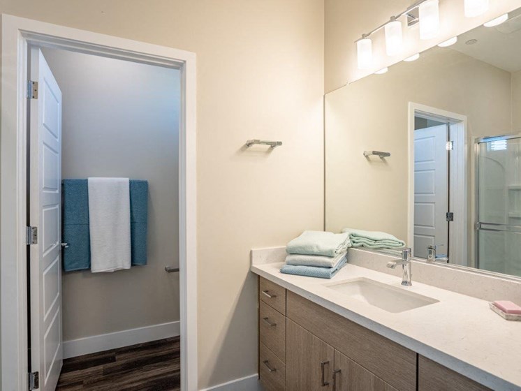 Model bathroom has a long mirrored vanity sink with storage in an apartment at Village Greens of Queen Creek