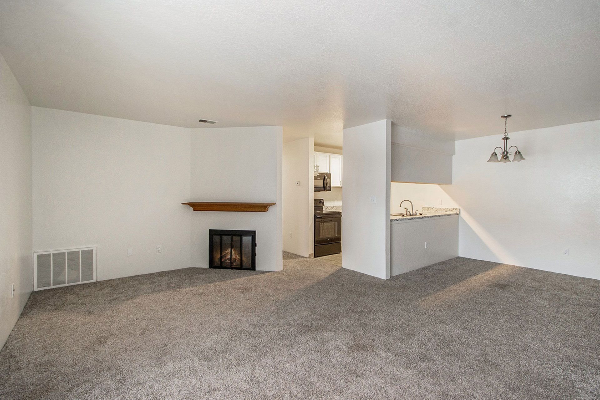 an empty living room with a fireplace and a kitchen