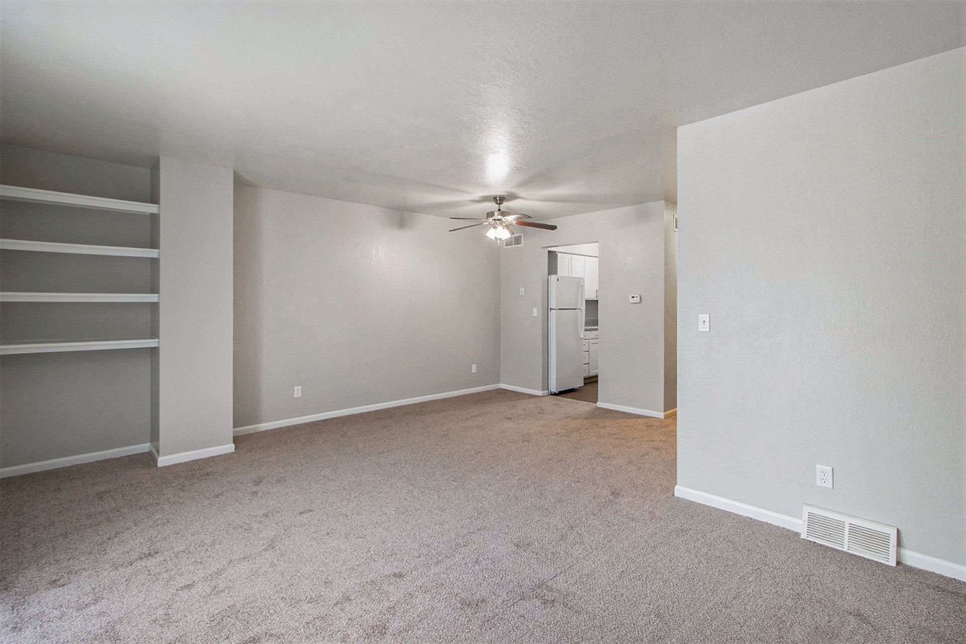 an empty living room with carpet and a ceiling fan