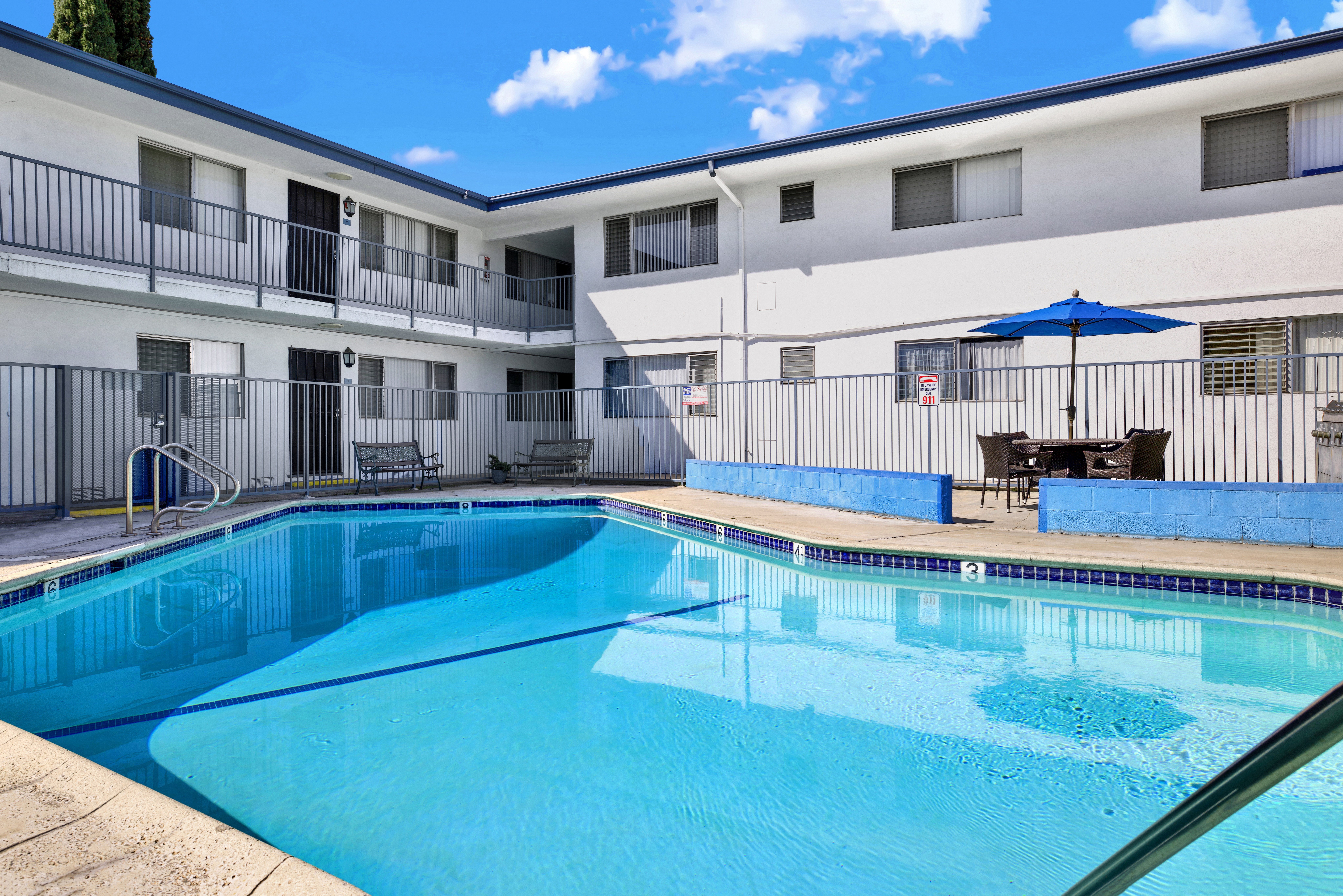 A swimming pool in front of a white building with blue umbrella.