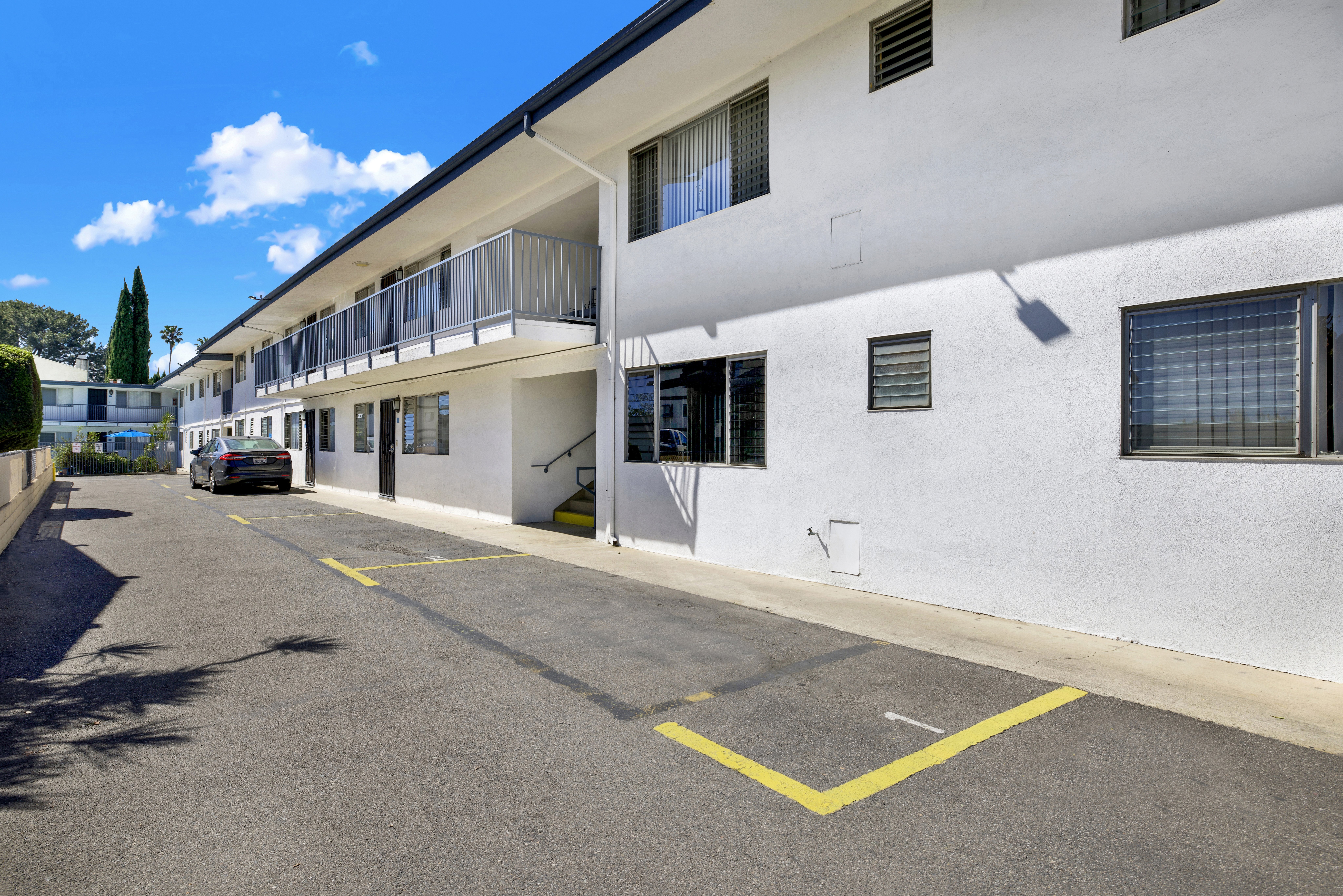 A parking lot in front of a white building with yellow lines on the ground.