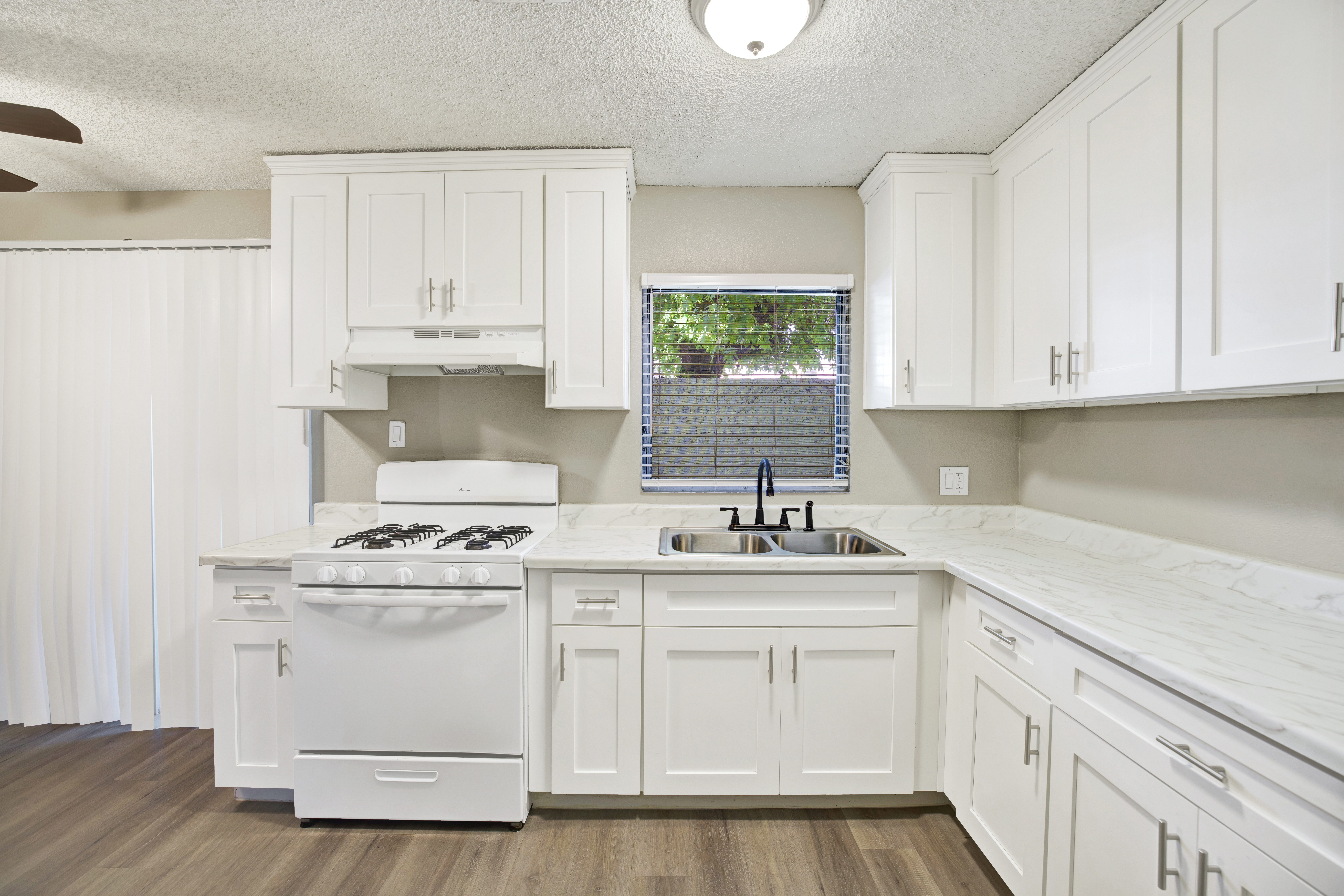 A white kitchen with a stove, sink, and cabinets.