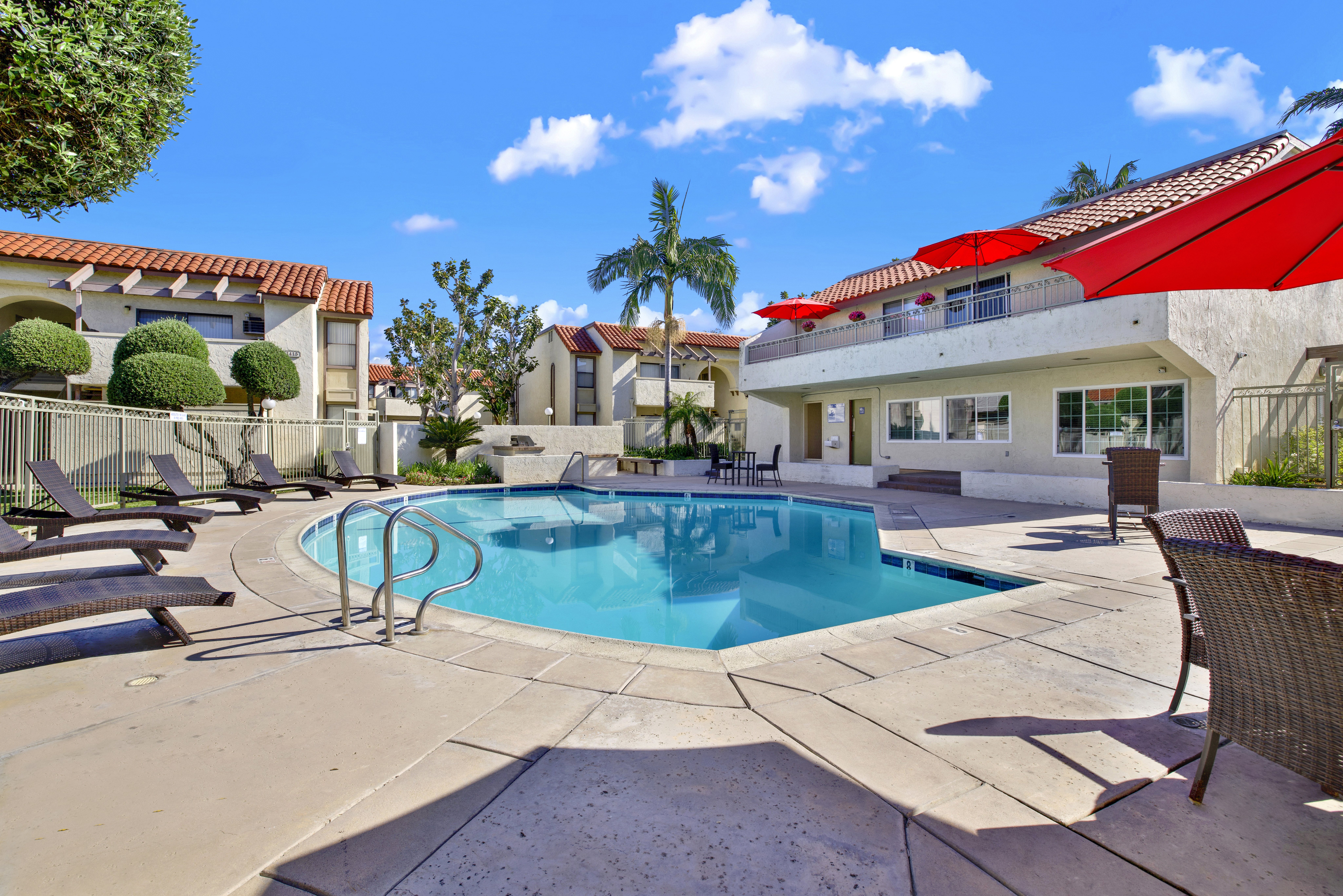 A pool surrounded by a patio and a red roofed building.