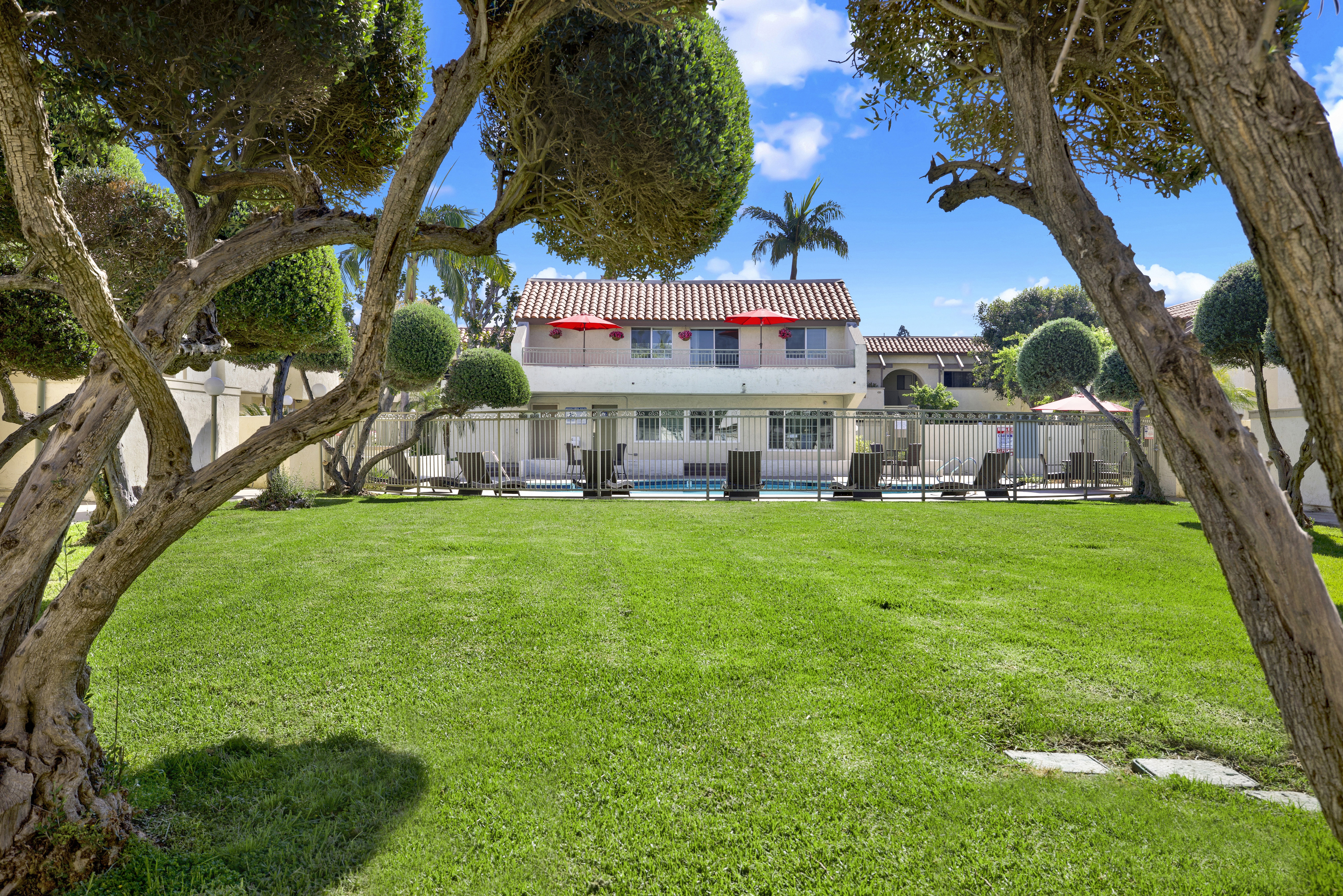 A house with a red roof is surrounded by a green lawn and trees.