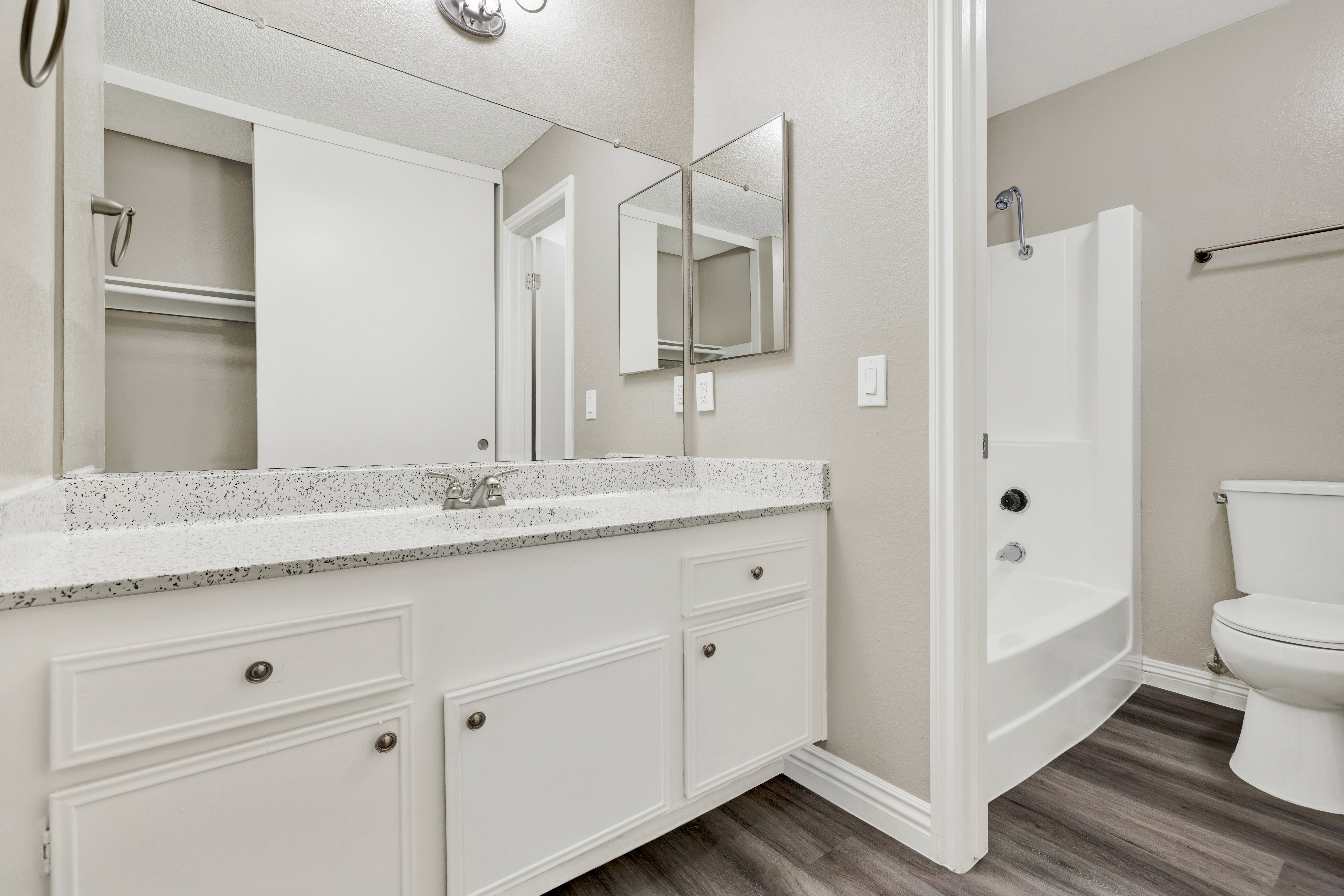 A white bathroom with a marble countertop and a walk-in shower.