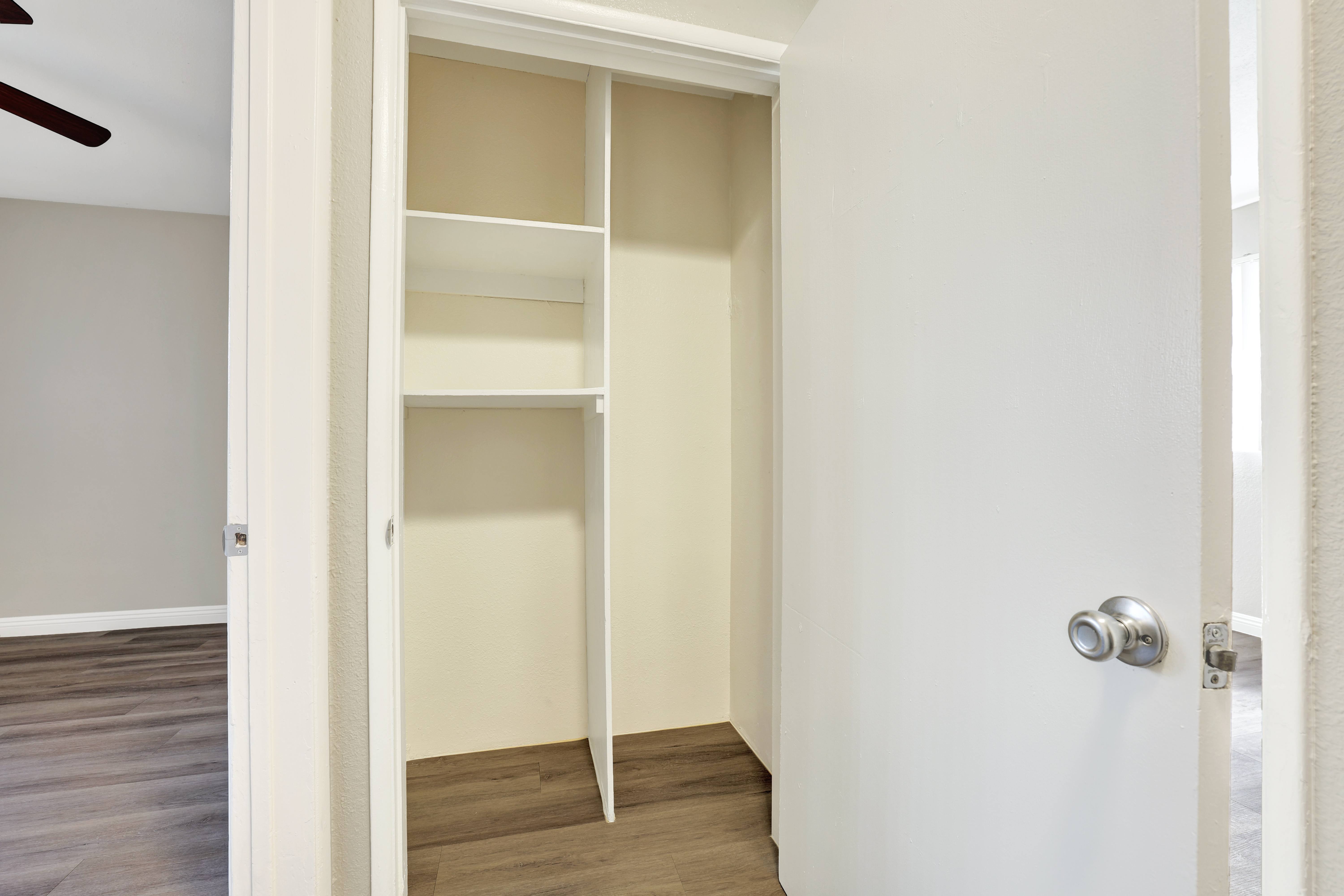 A white door with a silver handle is open to a room with a white wall and a wooden floor.
