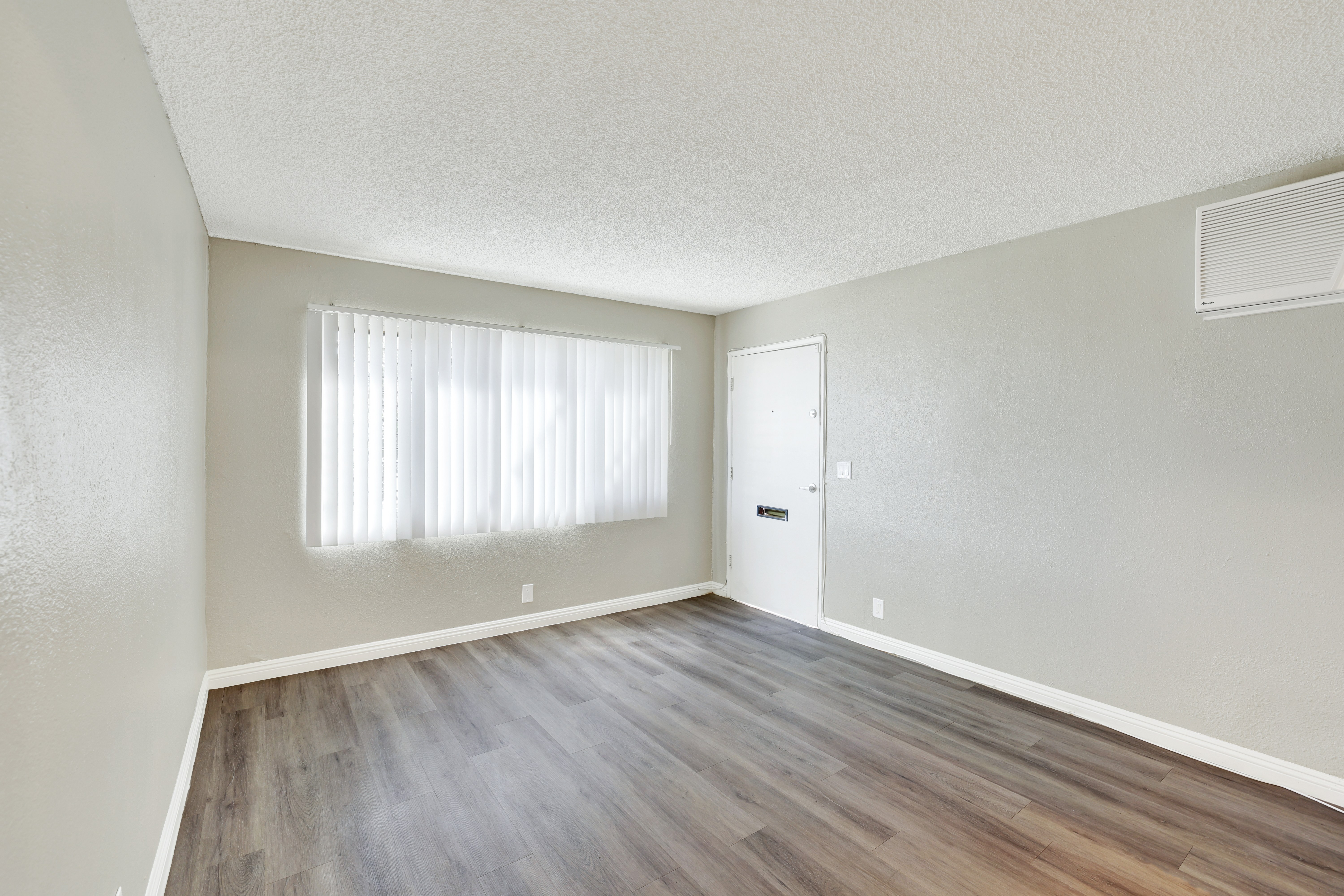 A room with a wooden floor and a window with white curtains.
