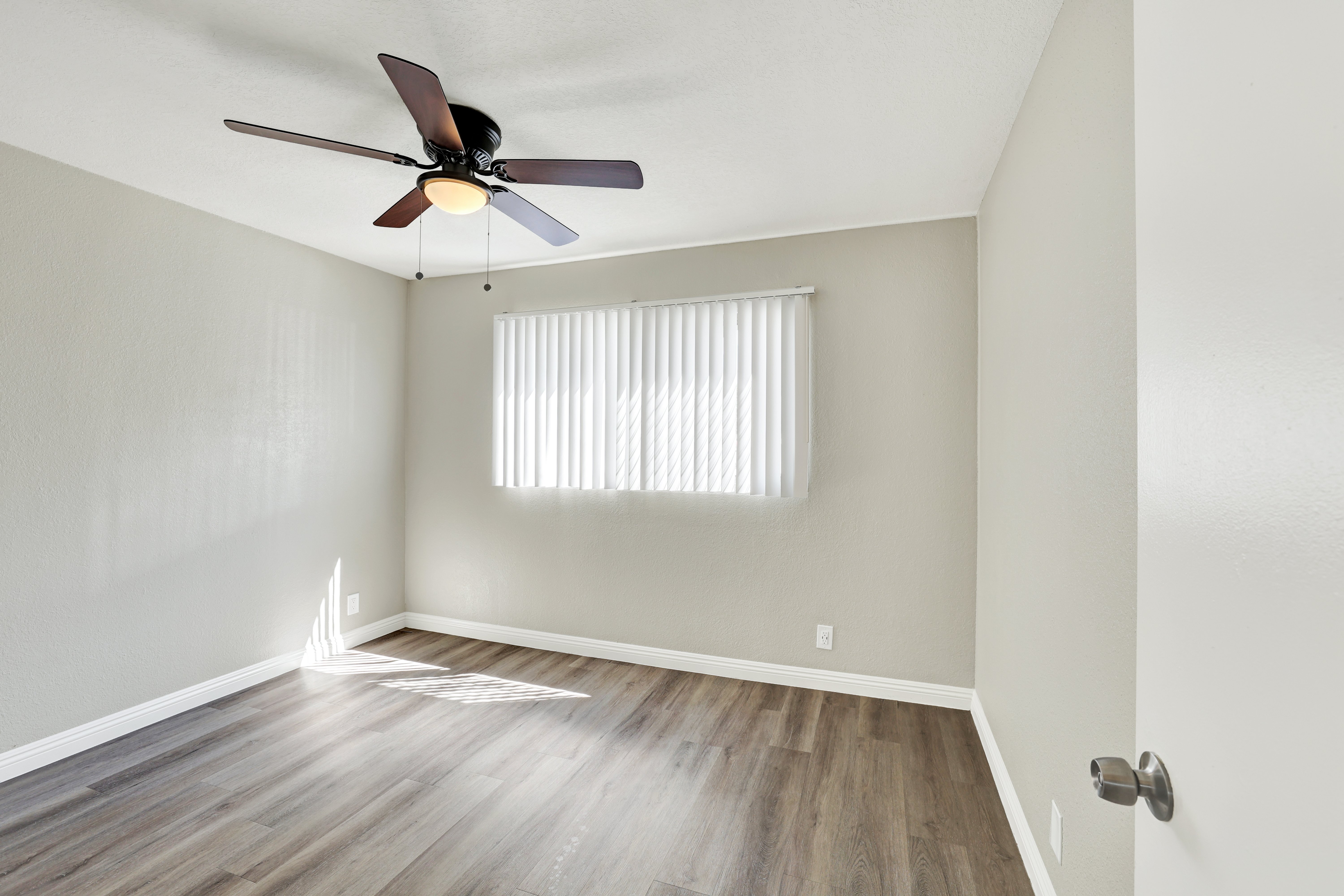 A room with a ceiling fan and a window with blinds.